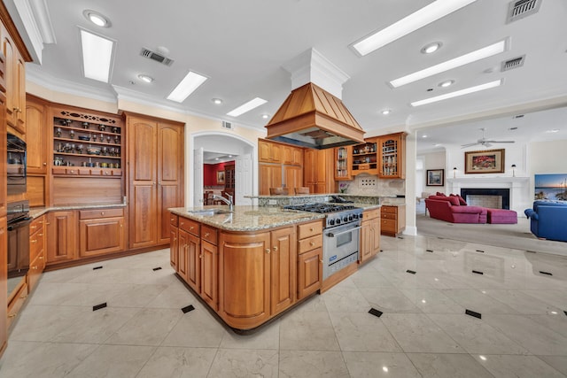 kitchen with light tile floors, high end stainless steel range, ceiling fan, and a center island with sink