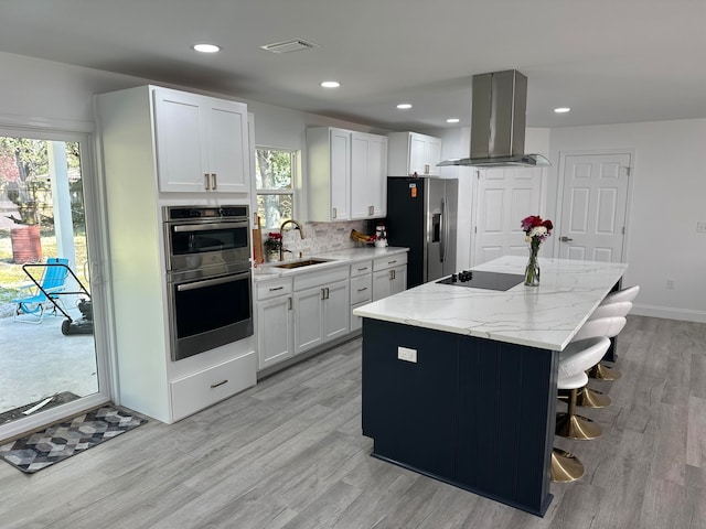 kitchen with island exhaust hood, appliances with stainless steel finishes, sink, white cabinets, and a center island