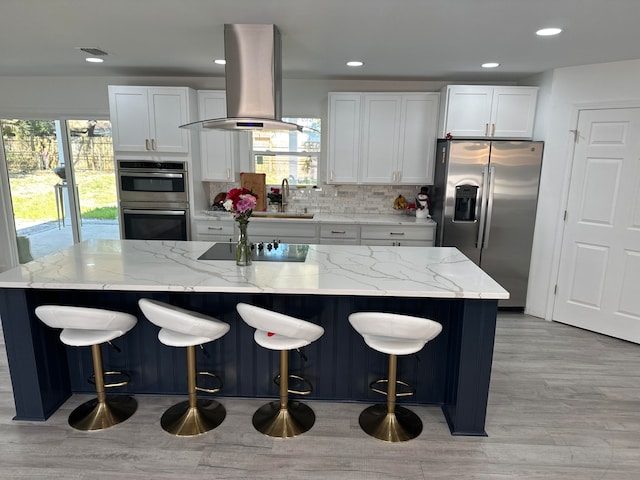 kitchen with island exhaust hood, appliances with stainless steel finishes, a center island, and white cabinetry