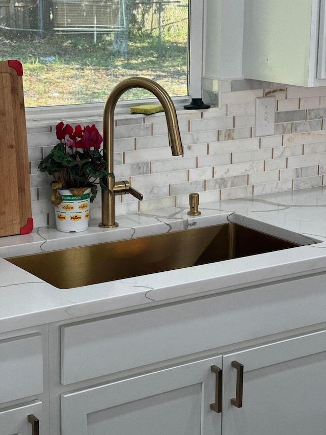 details with light stone countertops, backsplash, white cabinets, and sink