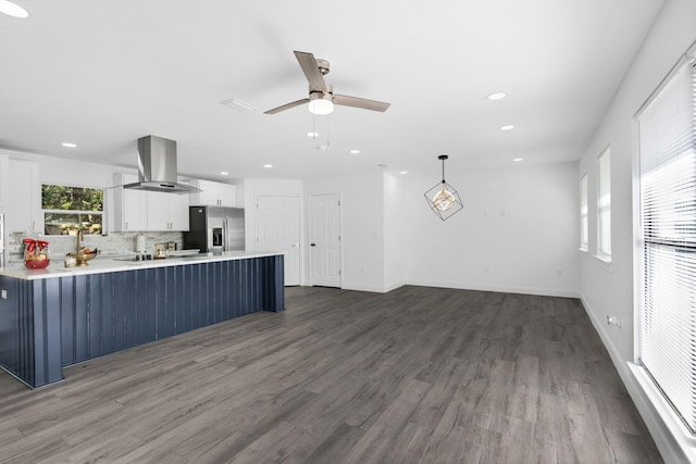 kitchen featuring white cabinets, wall chimney range hood, hanging light fixtures, stainless steel fridge, and wood-type flooring