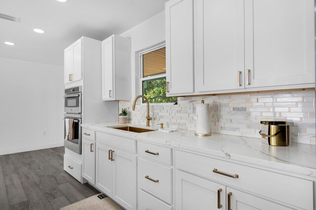 kitchen with light stone counters, stainless steel double oven, sink, hardwood / wood-style flooring, and white cabinets