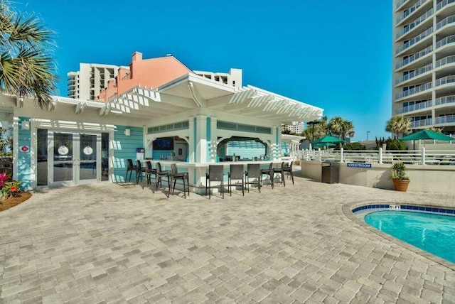 rear view of house featuring a community pool, an outdoor bar, and a patio