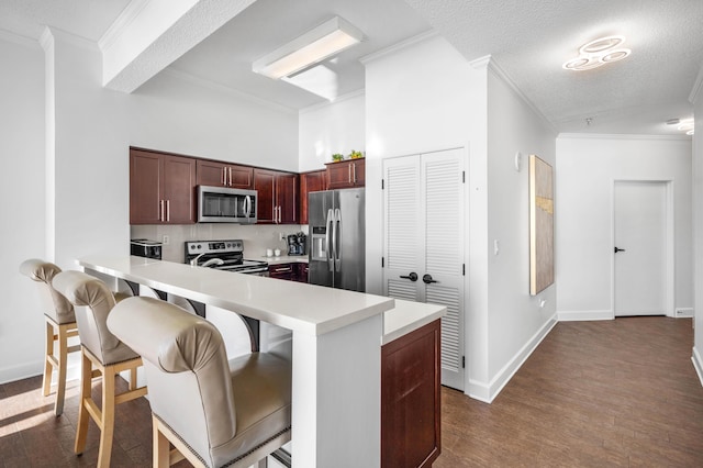 kitchen with a breakfast bar area, dark hardwood / wood-style floors, ornamental molding, a textured ceiling, and stainless steel appliances