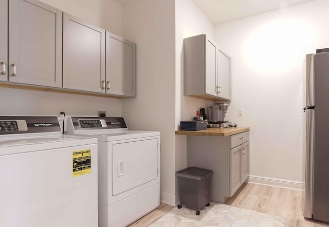 laundry area with cabinets, light wood-type flooring, and washer and clothes dryer