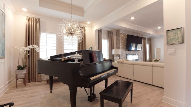 misc room featuring a chandelier, a stone fireplace, light wood-type flooring, and a tray ceiling