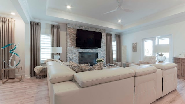 living room with ceiling fan, a fireplace, a raised ceiling, crown molding, and light hardwood / wood-style flooring