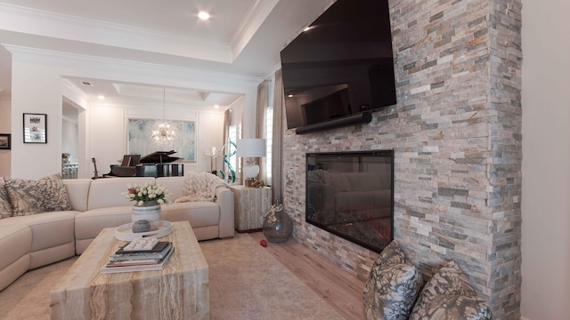 living room featuring light hardwood / wood-style floors, crown molding, a fireplace, a raised ceiling, and a notable chandelier