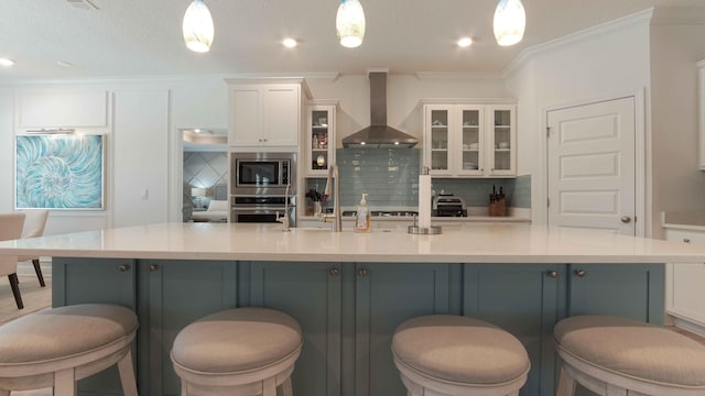 kitchen featuring appliances with stainless steel finishes, wall chimney range hood, backsplash, an island with sink, and pendant lighting