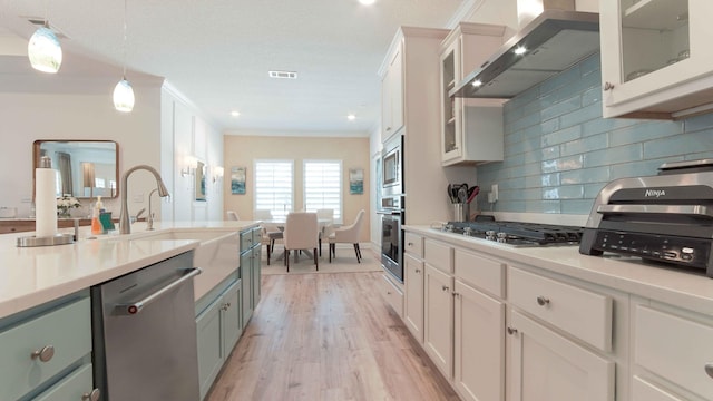 kitchen featuring decorative light fixtures, light hardwood / wood-style flooring, white cabinetry, wall chimney range hood, and stainless steel appliances