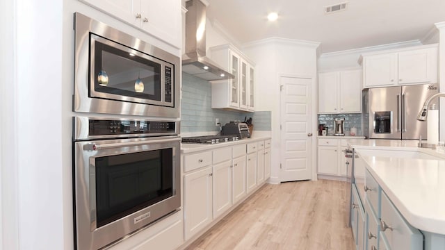 kitchen featuring tasteful backsplash, wall chimney exhaust hood, stainless steel appliances, and white cabinetry