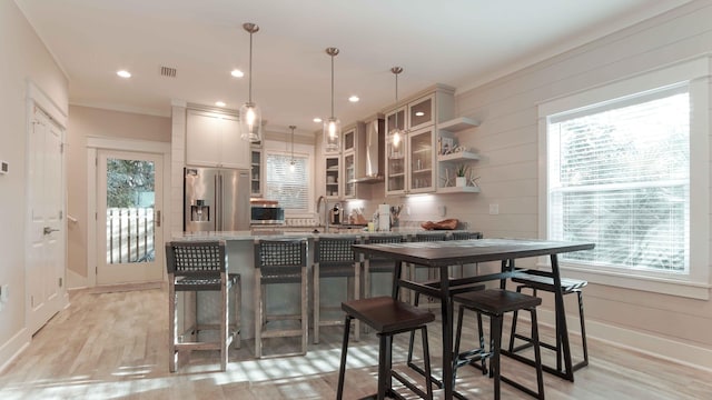 bar with decorative light fixtures, light stone countertops, appliances with stainless steel finishes, wall chimney range hood, and light hardwood / wood-style floors