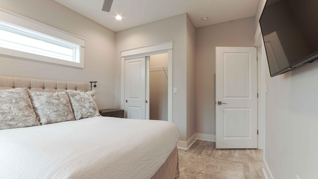 bedroom featuring a spacious closet, a closet, light hardwood / wood-style flooring, and ceiling fan