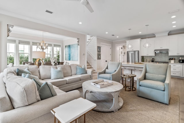 living room with ornamental molding, light hardwood / wood-style flooring, and ceiling fan with notable chandelier