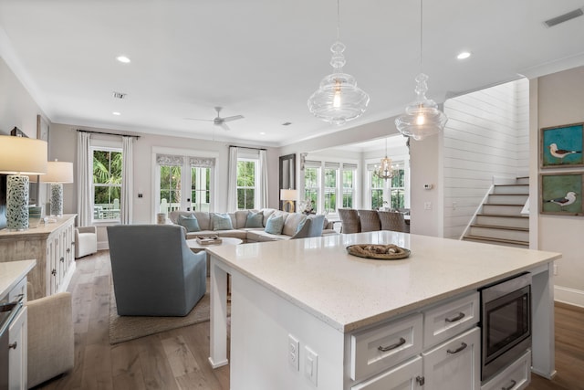 kitchen with white cabinets, light hardwood / wood-style flooring, a kitchen island, and stainless steel microwave