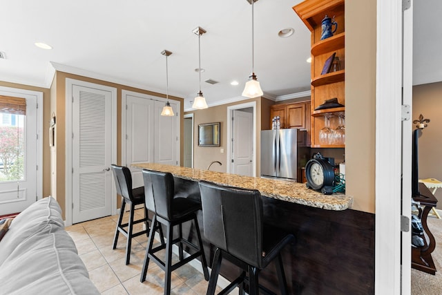 kitchen featuring light stone counters, light tile floors, decorative light fixtures, refrigerator, and a kitchen breakfast bar