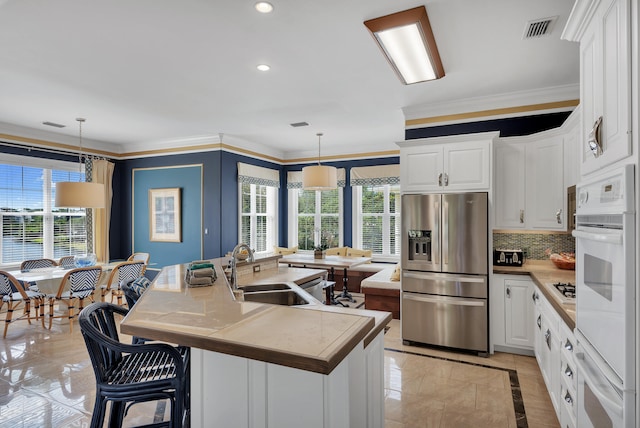 kitchen featuring pendant lighting, white cabinetry, an island with sink, and stainless steel fridge