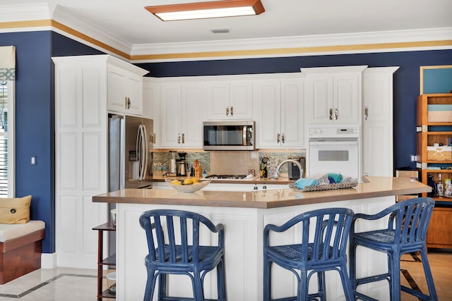 kitchen featuring a breakfast bar, crown molding, white cabinetry, backsplash, and stainless steel appliances