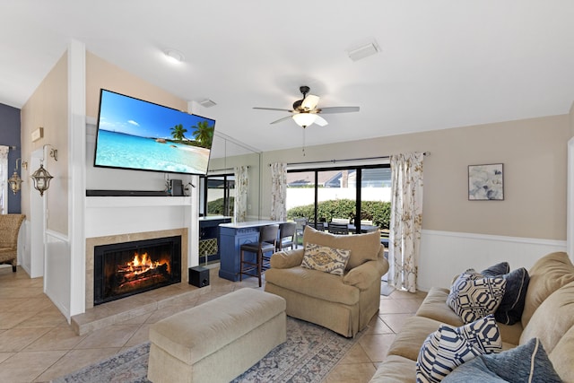 living area with light tile patterned floors, ceiling fan, vaulted ceiling, wainscoting, and a tiled fireplace