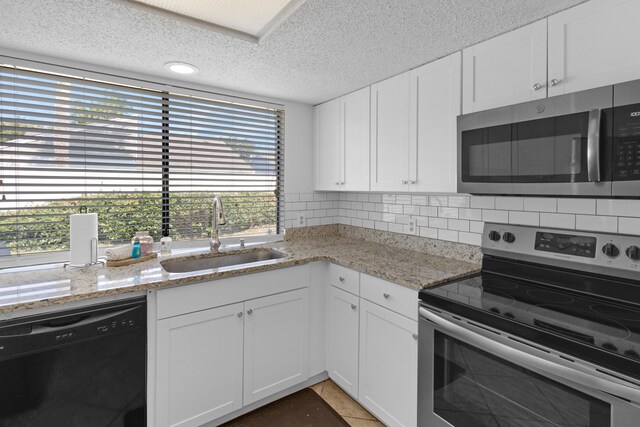 kitchen featuring tile patterned floors, appliances with stainless steel finishes, white cabinetry, sink, and decorative backsplash