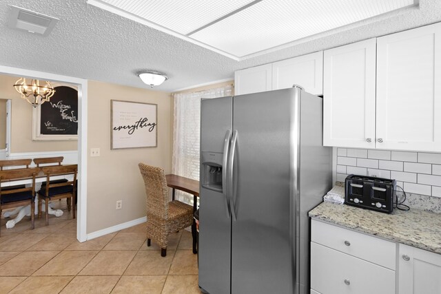 kitchen featuring a textured ceiling, light tile patterned floors, decorative backsplash, white cabinets, and stainless steel fridge