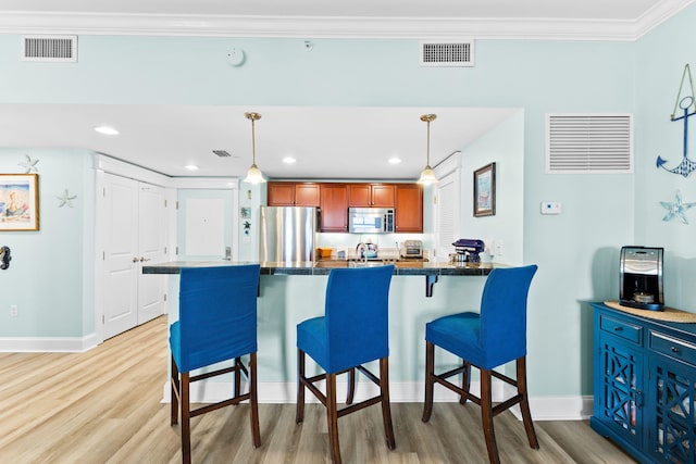 kitchen with appliances with stainless steel finishes, a breakfast bar, pendant lighting, and light wood-type flooring