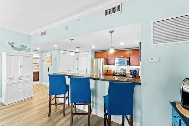 kitchen featuring a breakfast bar area, decorative light fixtures, light hardwood / wood-style flooring, ornamental molding, and stainless steel appliances