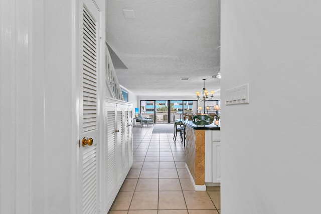 hallway with light tile patterned flooring, an inviting chandelier, and a textured ceiling