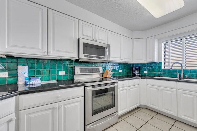 kitchen featuring light tile patterned flooring, appliances with stainless steel finishes, white cabinetry, sink, and decorative backsplash