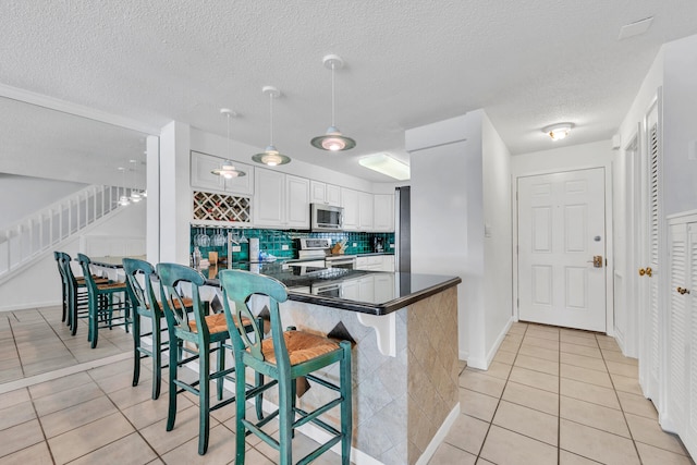 kitchen with appliances with stainless steel finishes, white cabinets, a kitchen bar, decorative light fixtures, and kitchen peninsula