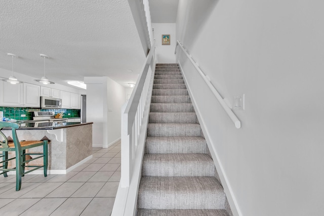 stairs featuring tile patterned flooring, ceiling fan, and a textured ceiling