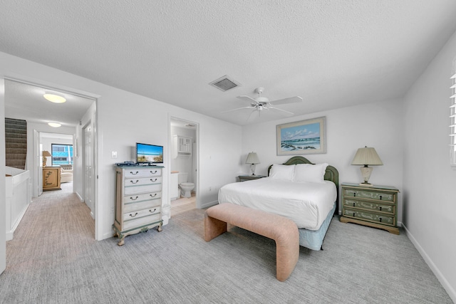 bedroom with ceiling fan, connected bathroom, light carpet, and a textured ceiling