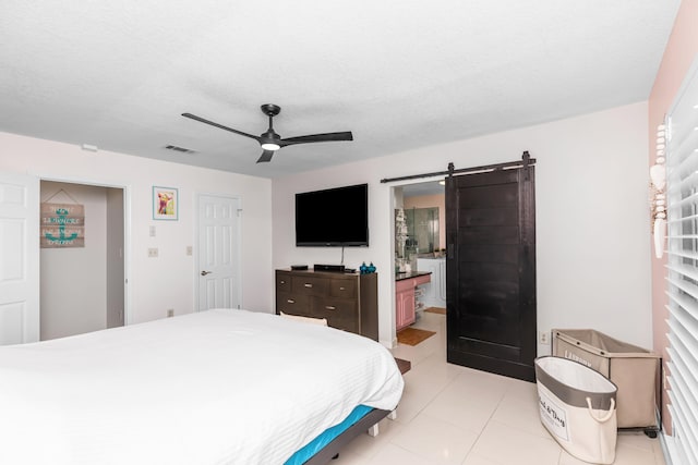 tiled bedroom with ceiling fan, a barn door, a textured ceiling, and ensuite bath