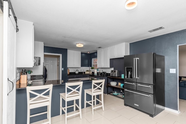 kitchen with white cabinetry, kitchen peninsula, high end fridge, light tile patterned flooring, and a breakfast bar area