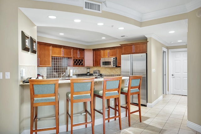 kitchen with crown molding, appliances with stainless steel finishes, light tile floors, a breakfast bar area, and tasteful backsplash