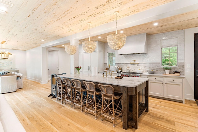 kitchen with light stone counters, a kitchen island with sink, backsplash, and pendant lighting