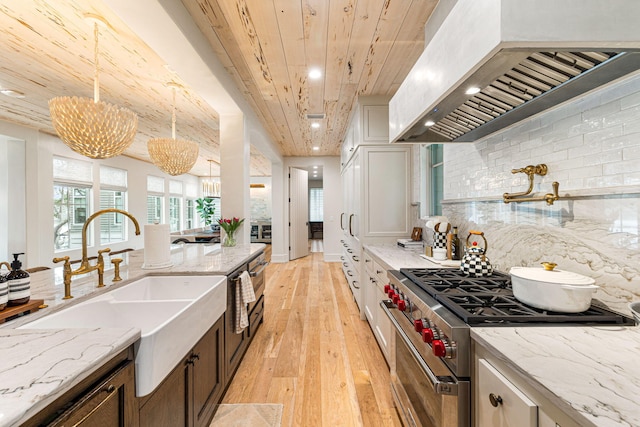 kitchen with hanging light fixtures, white cabinets, custom range hood, tasteful backsplash, and premium range