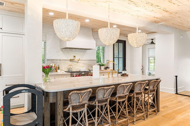 kitchen with plenty of natural light, custom exhaust hood, pendant lighting, and light stone countertops