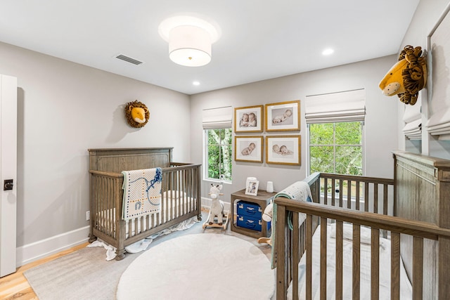 bedroom featuring light hardwood / wood-style floors, a crib, and multiple windows