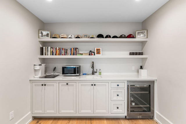 bar with wine cooler, sink, light hardwood / wood-style flooring, and white cabinetry