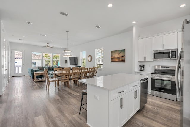 kitchen featuring decorative light fixtures, light hardwood / wood-style flooring, stainless steel appliances, white cabinets, and a center island