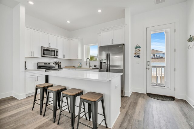 kitchen featuring a center island, stainless steel appliances, white cabinets, and light wood-type flooring