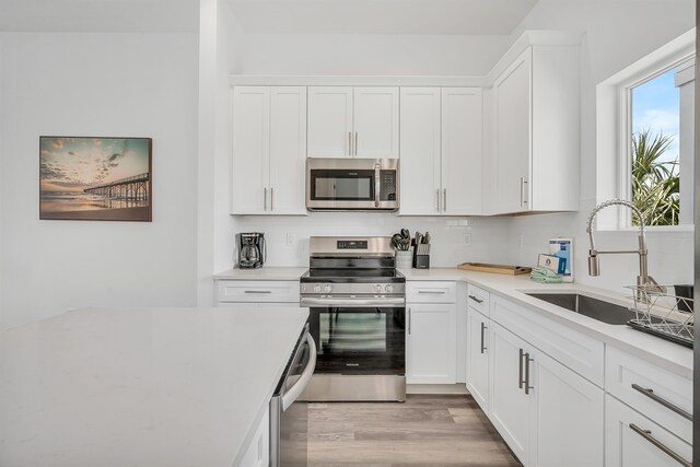 kitchen featuring appliances with stainless steel finishes, white cabinets, sink, light hardwood / wood-style floors, and tasteful backsplash