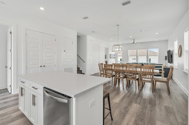 kitchen with hanging light fixtures, a kitchen island, light hardwood / wood-style floors, white cabinets, and stainless steel dishwasher