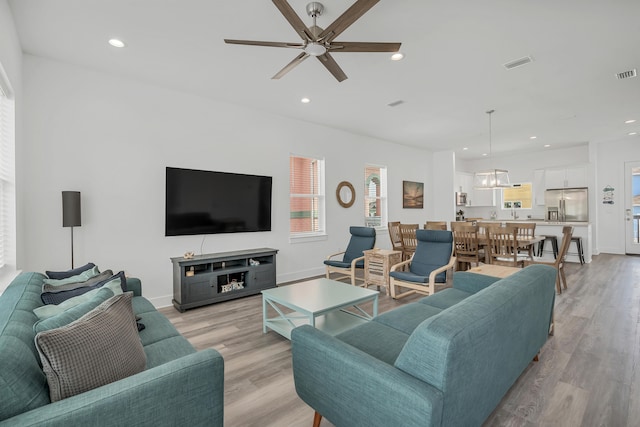 living room with light hardwood / wood-style floors and ceiling fan with notable chandelier