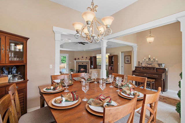 dining space featuring light tile patterned flooring, a tile fireplace, ceiling fan with notable chandelier, and decorative columns