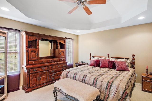 bedroom with a raised ceiling, light colored carpet, and ceiling fan