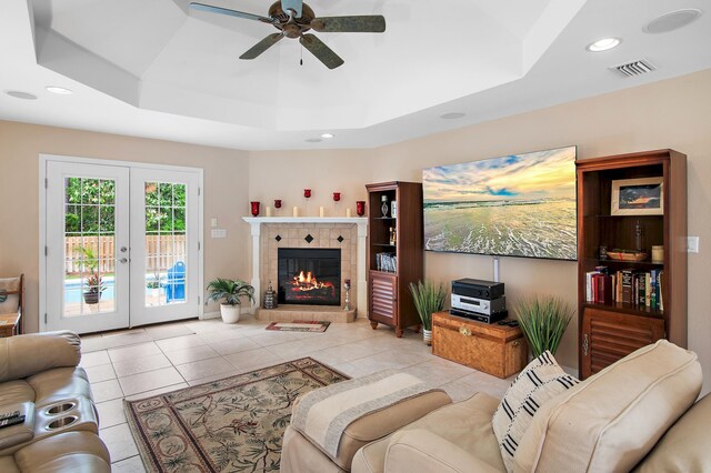 tiled living room featuring french doors, ceiling fan, a tray ceiling, and a fireplace