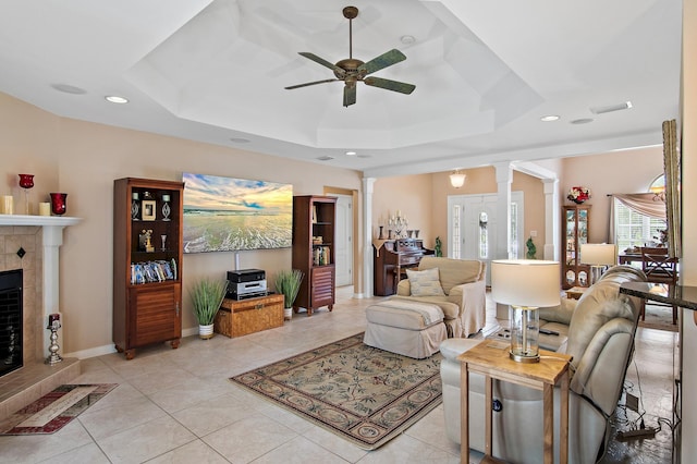 tiled living room with ceiling fan, decorative columns, a tray ceiling, and a tile fireplace