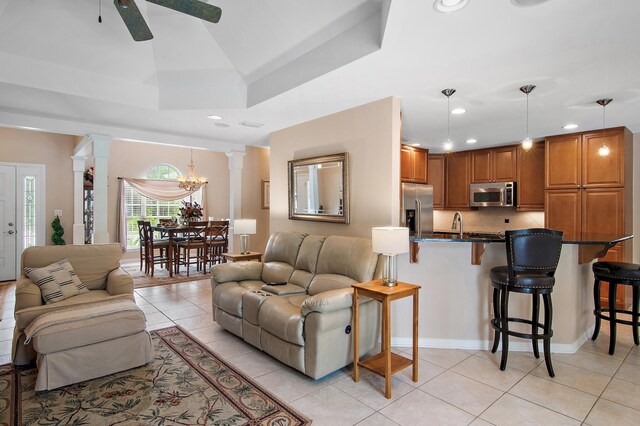 tiled living room featuring ornate columns and ceiling fan with notable chandelier